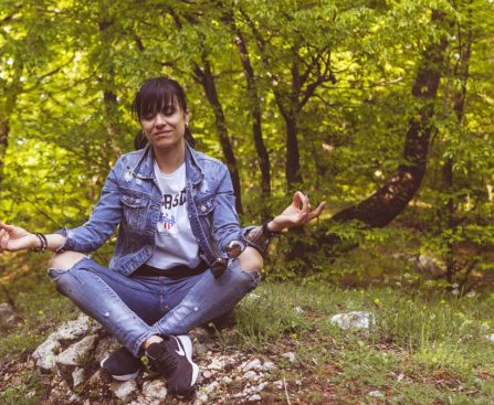 A woman meditates peacefully in a lush green forest, exuding calm and relaxation.